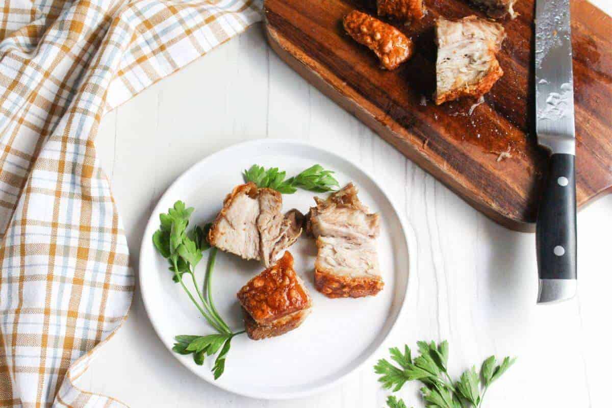 Pork belly bites on a plate and cutting board with a knife.