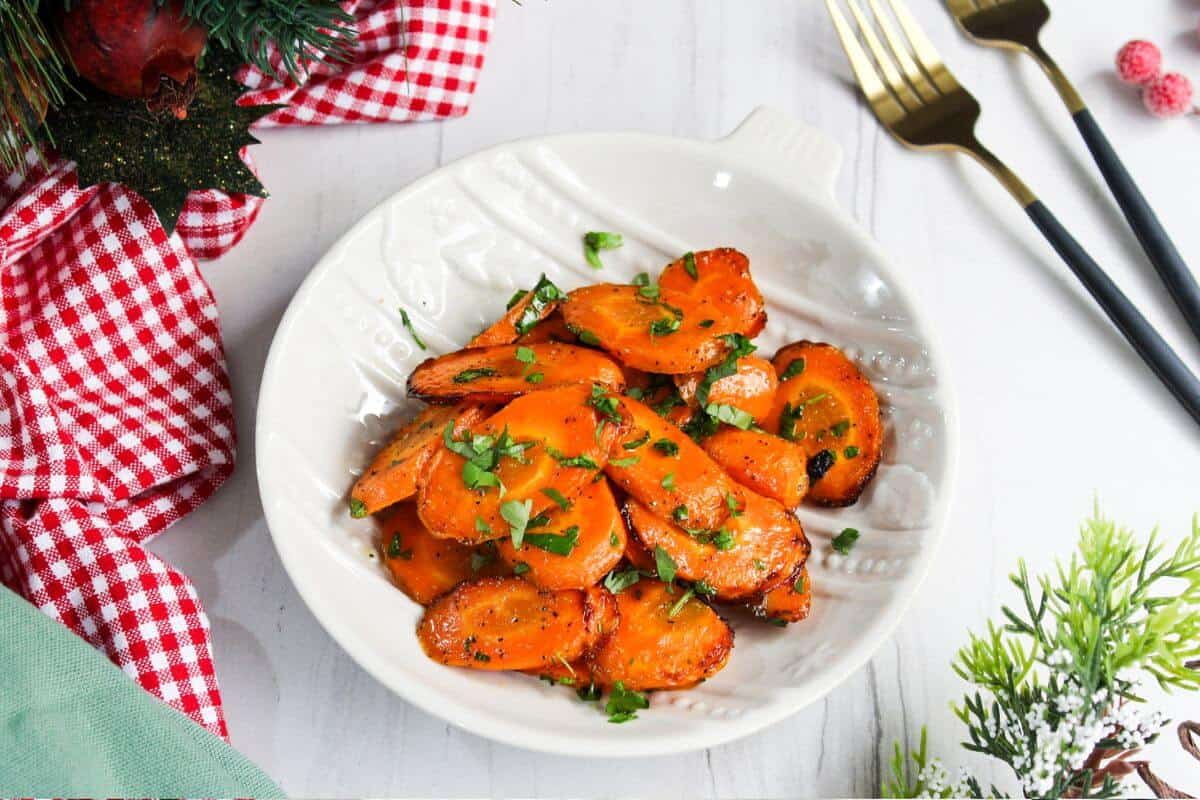 Air fried glazed carrots in a white bowl next to a checkered tablecloth.