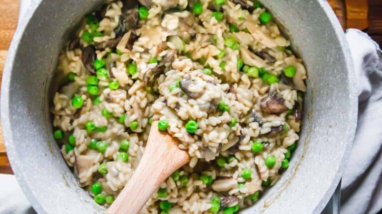 Mushroom and pea risotto in a pan with a wooden spoon.