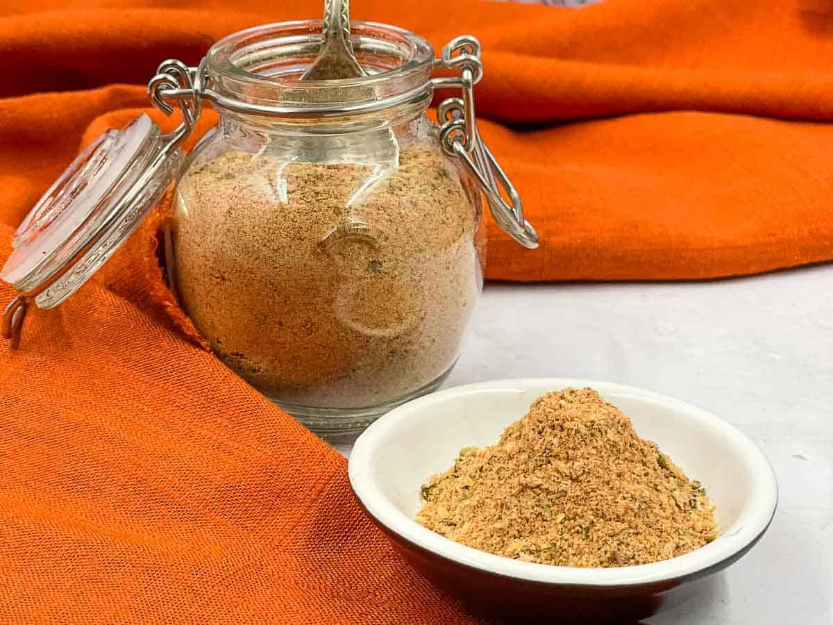 A jar of Peri Peri Seasoning and a bowl on an orange cloth.