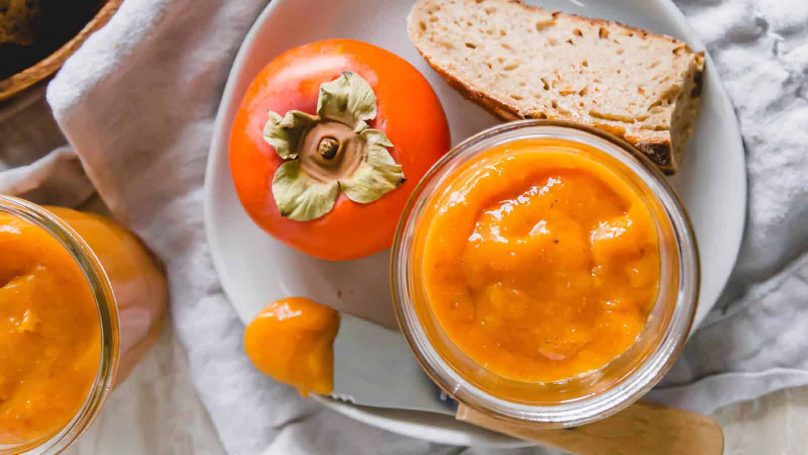 Two jars of persimmon jam on a white plate.