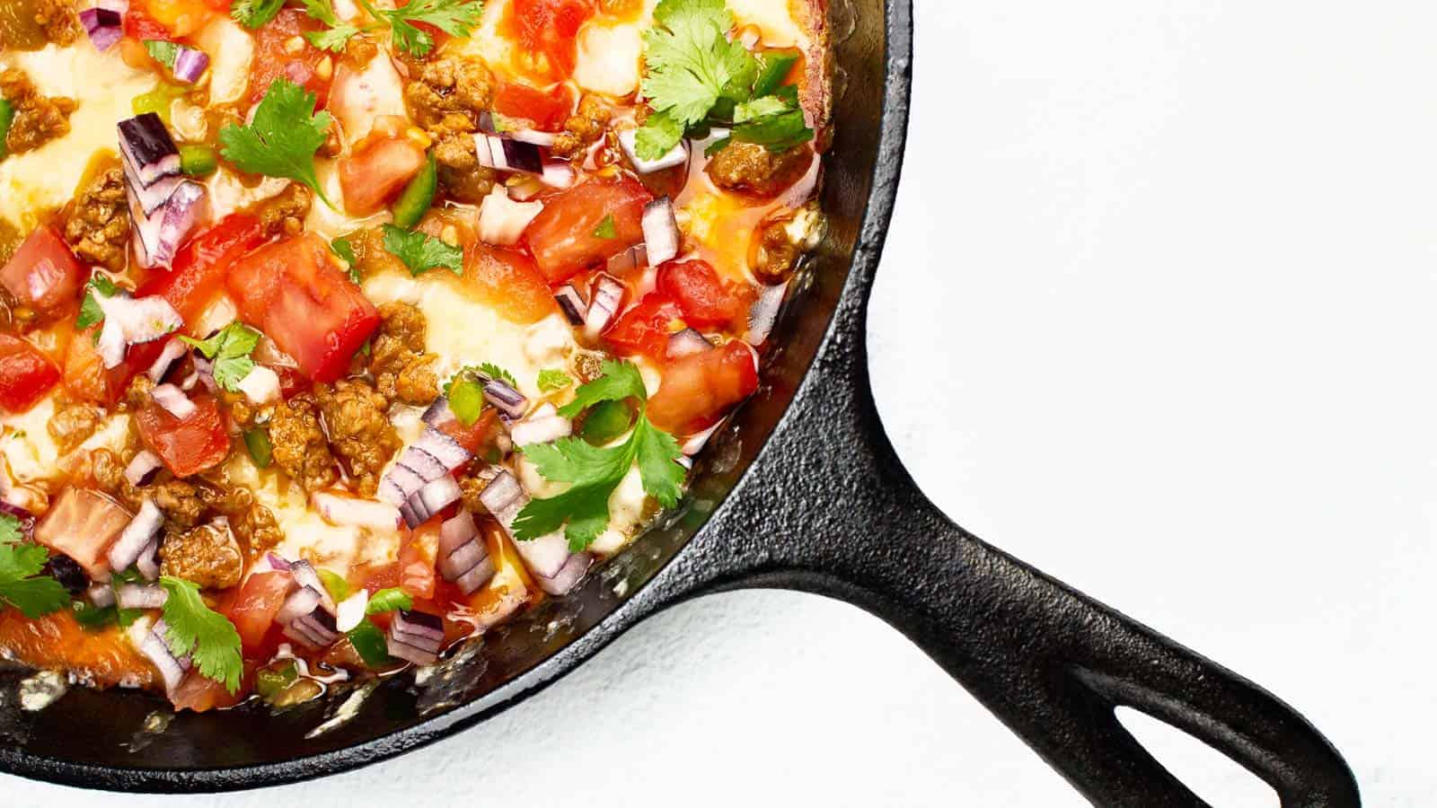 A black skillet of cheesy dip and coveredin pico de gallo.