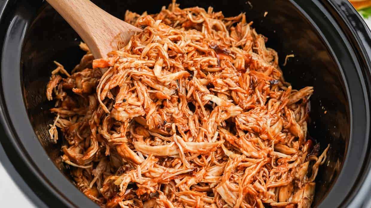 Slow cooker chicken with BBQ sauce in a crock pot with a spoon.