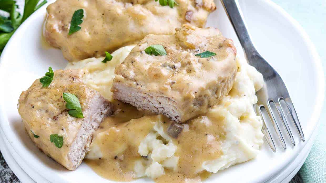 Slow Cooker Pork Chops on a plate covered with a creamy mushroom gravy and served on mashed potatoes.