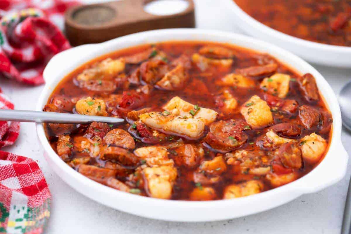 A bowl of soup with sausage and fish.