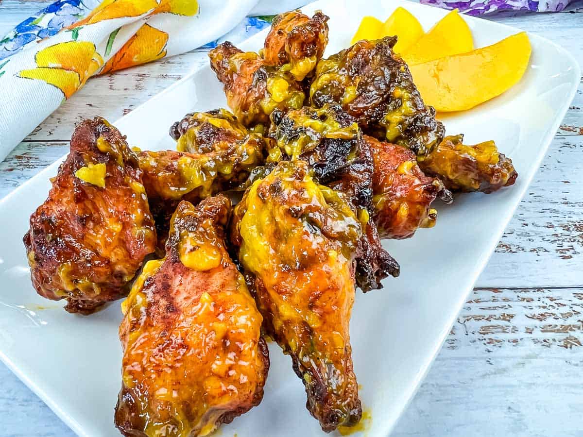 A plate of chicken wings on a white plate with a slice of mango.