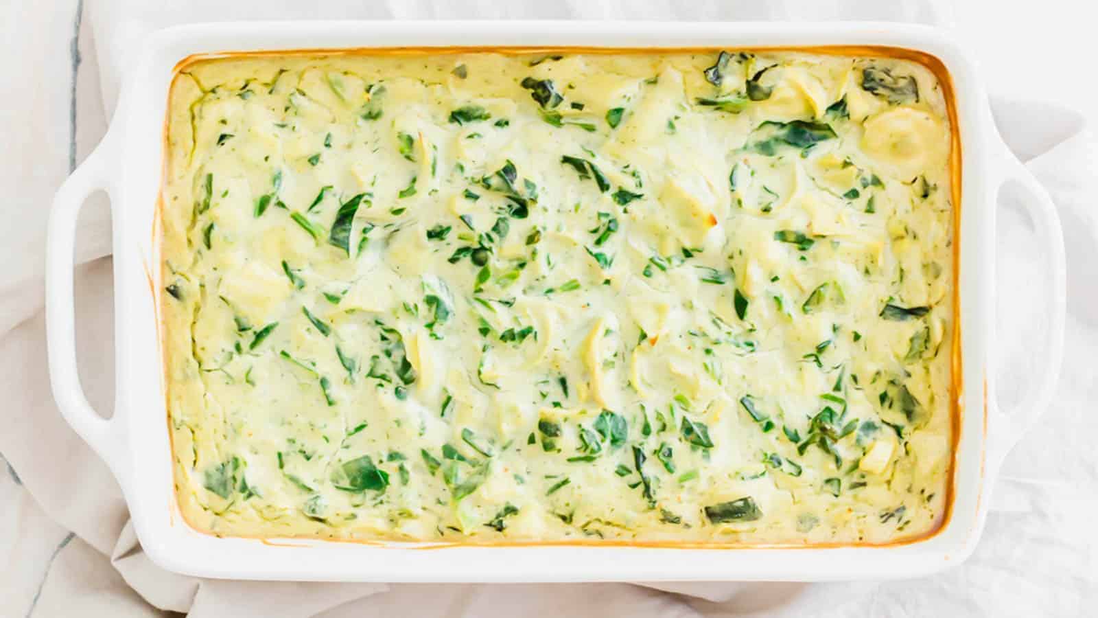 Spinach artichoke dip in a white baking dish.