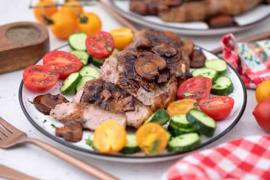 A plate with steak, tomatoes and cucumbers on it.