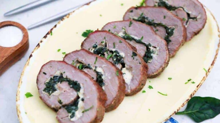 A plate with sliced meat and spinach on it.