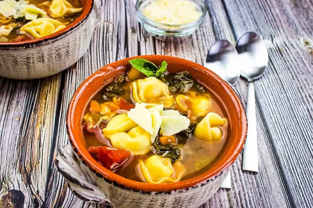 Two bowls of tortellini soup that taste better on a wooden table.