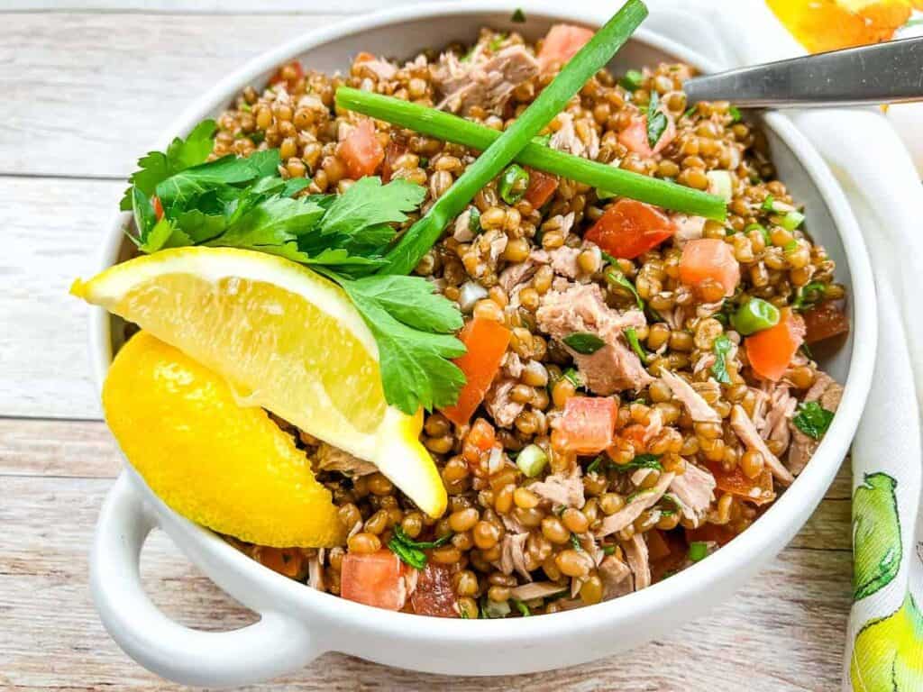 A bowl of tuna farro salad with lemon wedges.