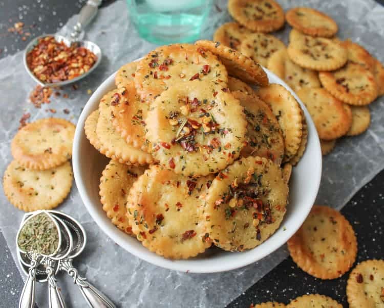 A bowl of spicy, seasoned crackers with a mess of ingredients around it.