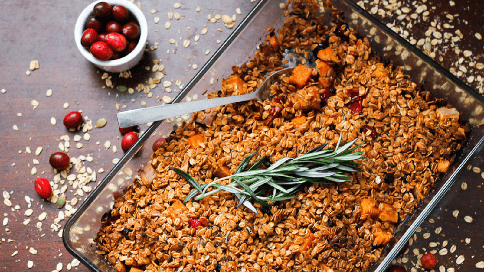 A cozy dish of granola with cranberries and sprigs of rosemary.