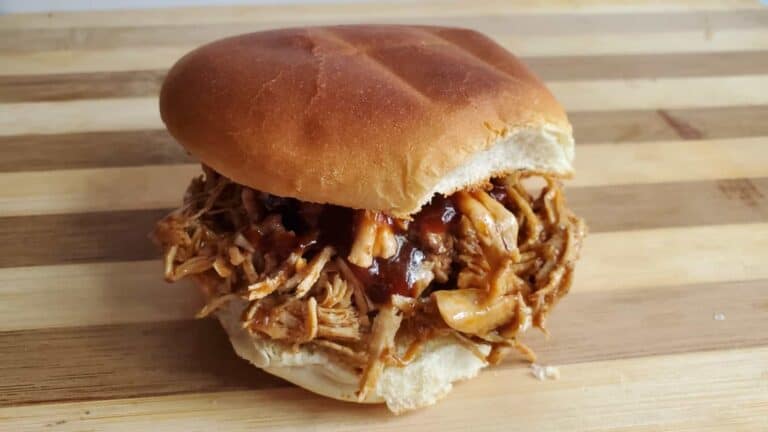 Image shows a shredded bbq chicken sandwich on a wooden board.