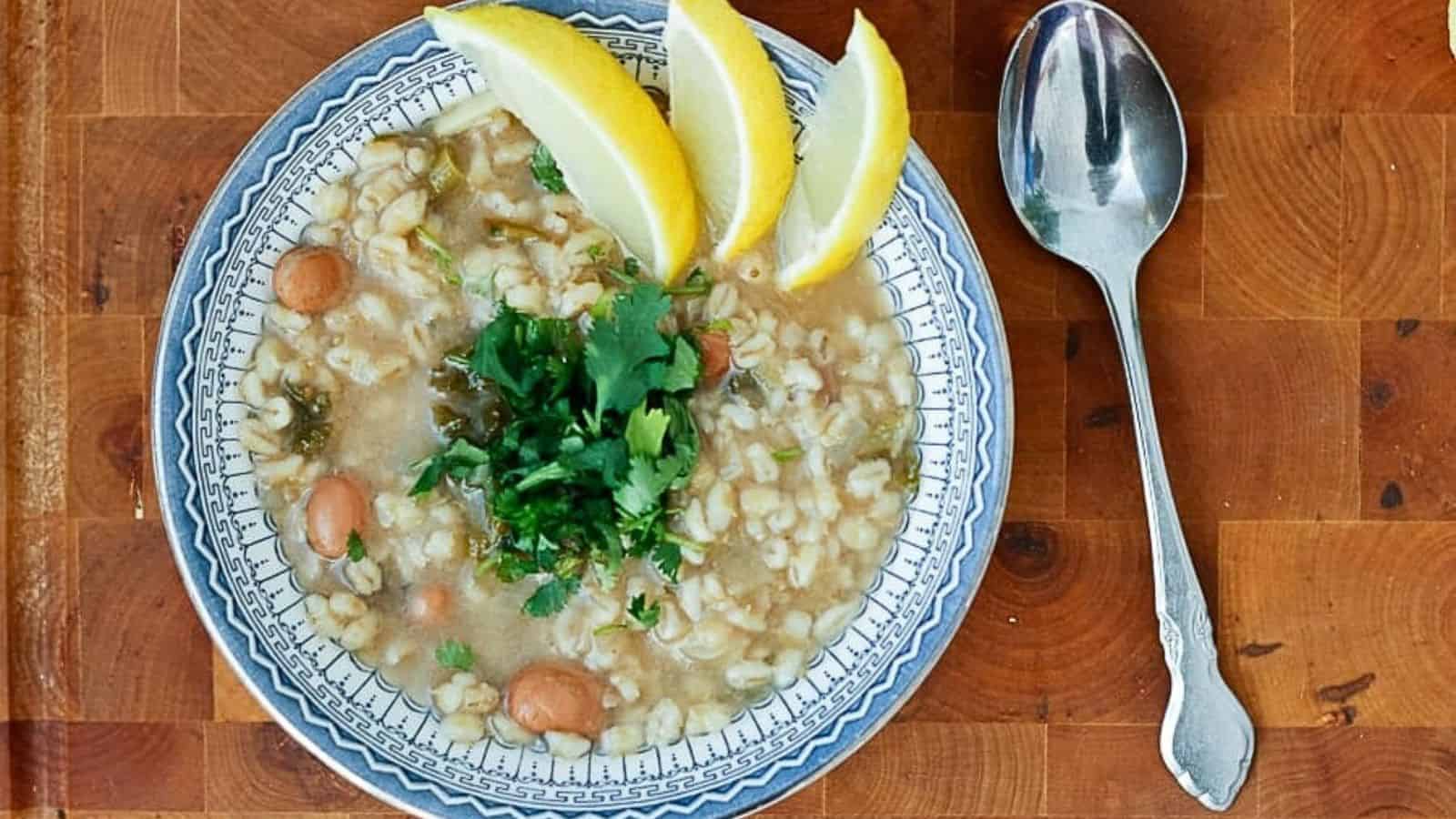 A bowl of soup with a spoon and lemon wedges.