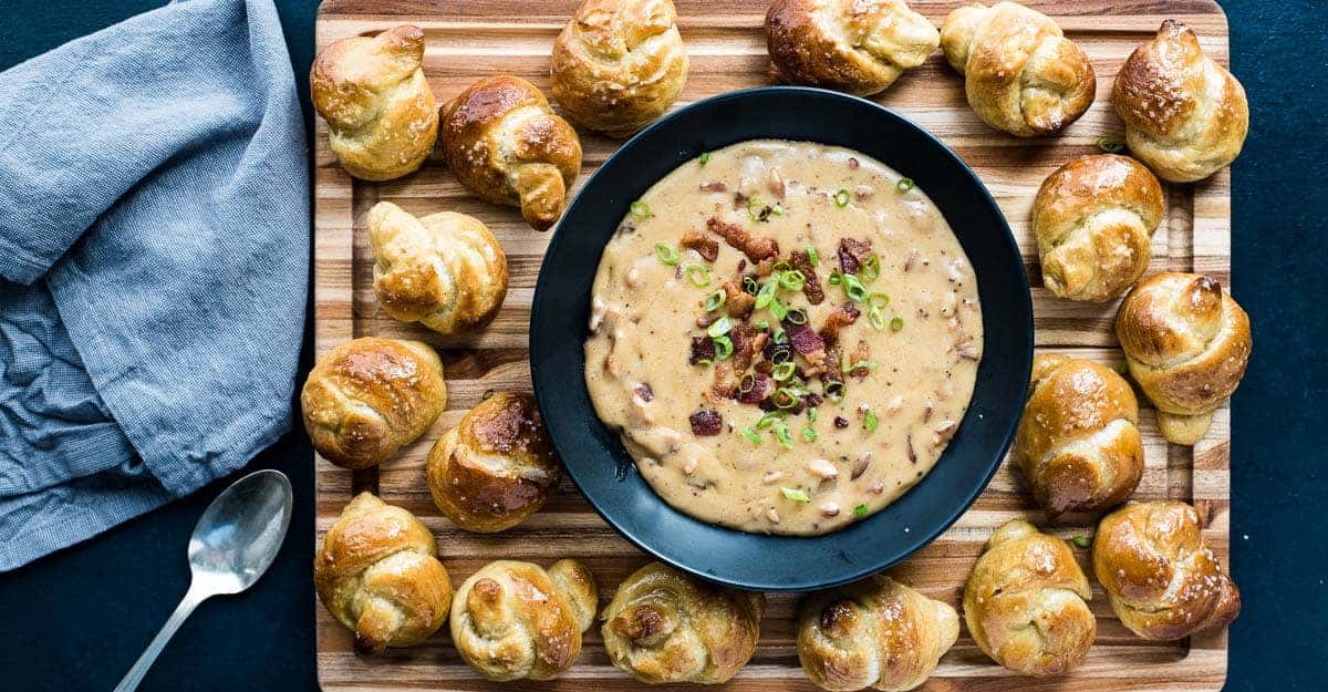 A holiday appetizer featuring a bowl of soup on a wooden cutting board.