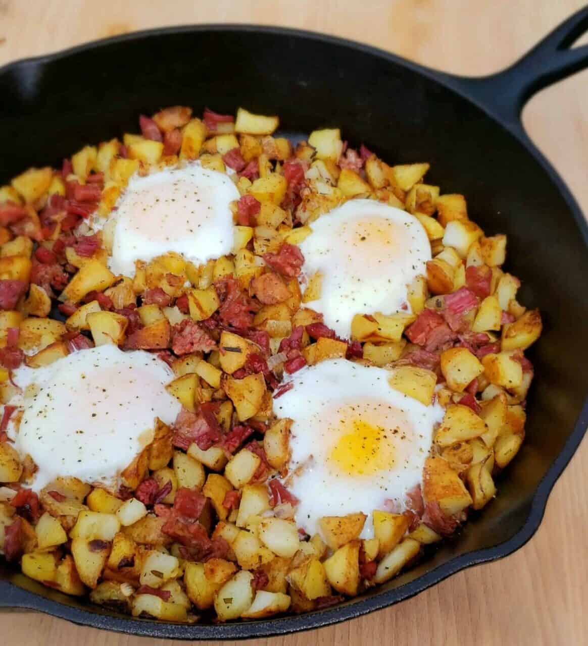 Cast iron skillet with corned beef hash and four shirred eggs.