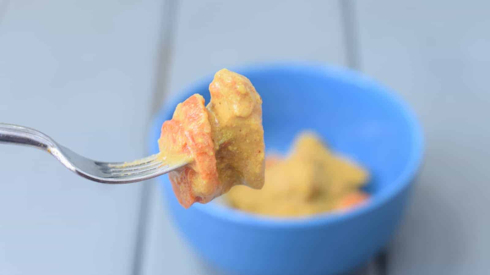 Image shows a Bite of chicken curry on a fork with the rest of the bowl in the background.