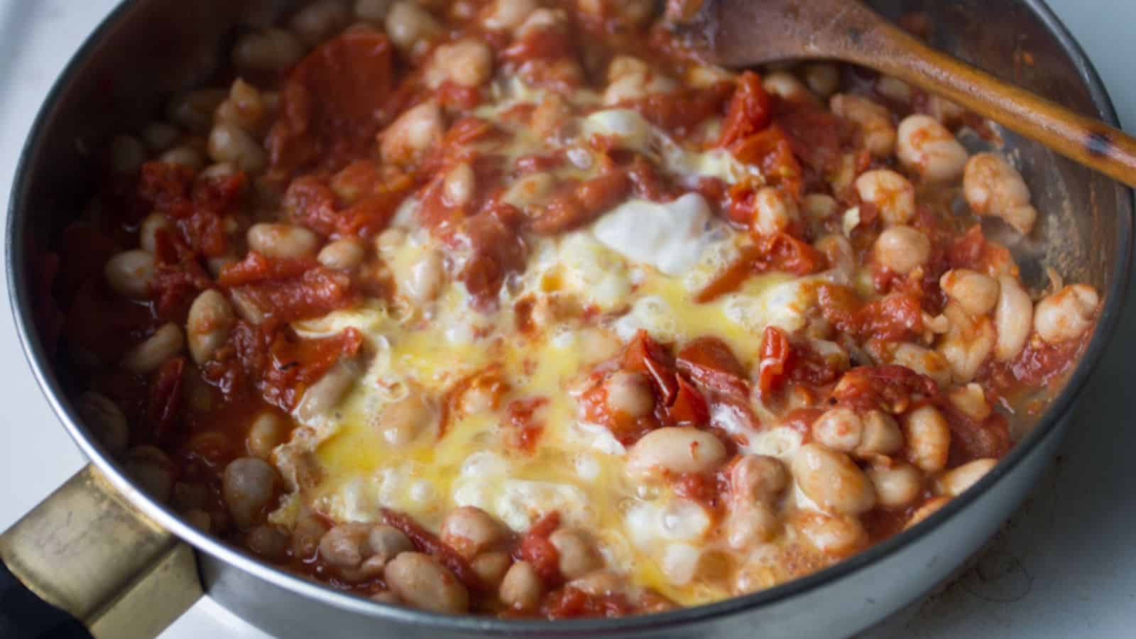 White beans and tomatoes, two essential ingredients for veggie mains, simmer together beautifully in a pan. Stirring it all with a trusty wooden spoon adds the finishing touch to this delicious dish.