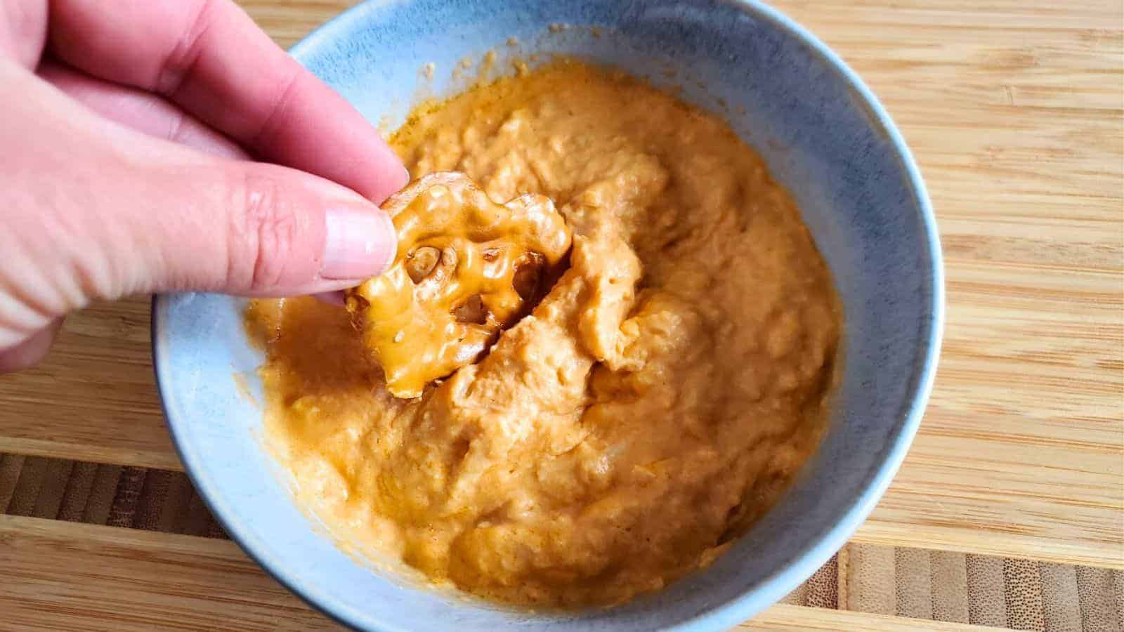 Image shows A person dipping a pretzel crisp into a bowl of buffalo chicken dip.