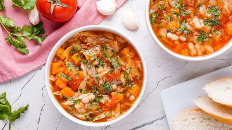 Two bowls of cabbage soup with bread slices on the side.