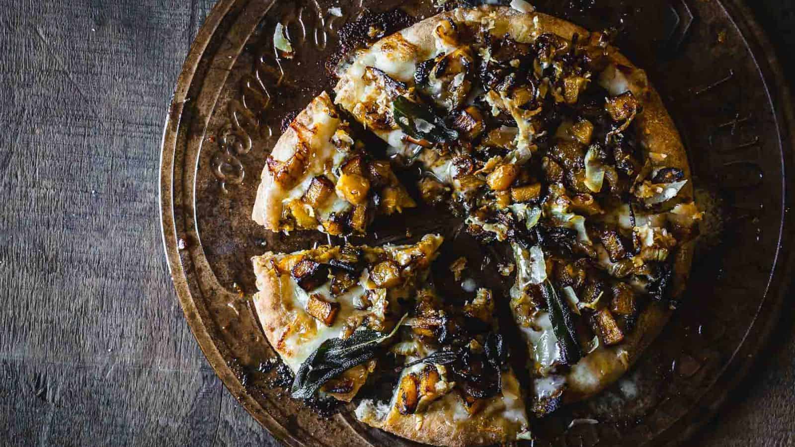 A vegetarian pizza topped with onions and sage, served on a rustic wooden board.