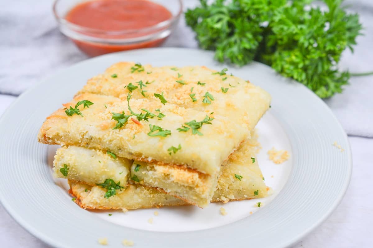 Cheesy bread sticks with marinara sauce and parsley on a plate.