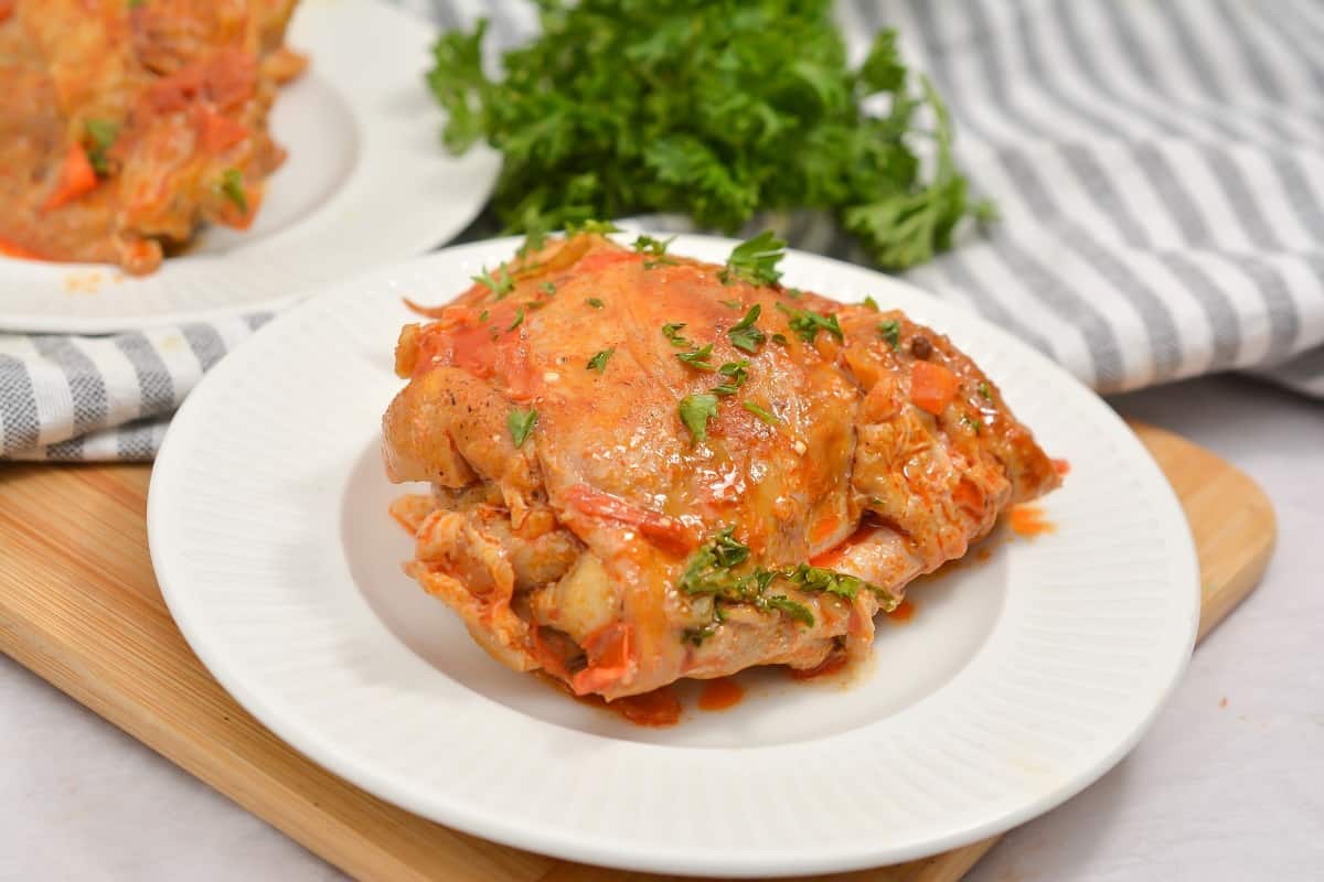 A plate of chicken with sauce and parsley on a cutting board.