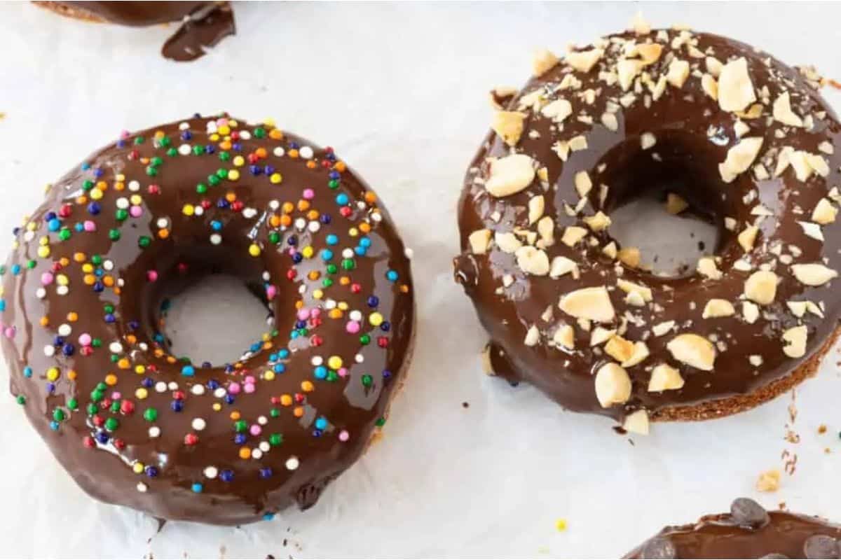 Three chocolate donuts with sprinkles and chocolate icing.