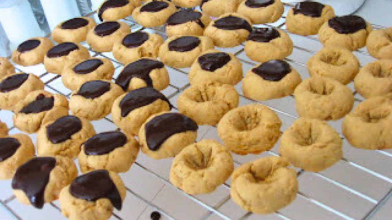 Image shows a cooling rack with orange shortbread cookies half filled with chocolate ganache and half not.