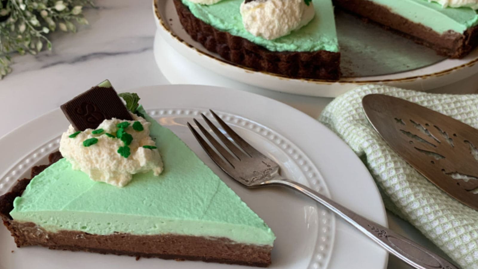 Chocolate mint tart slice on a white plate with a fork.