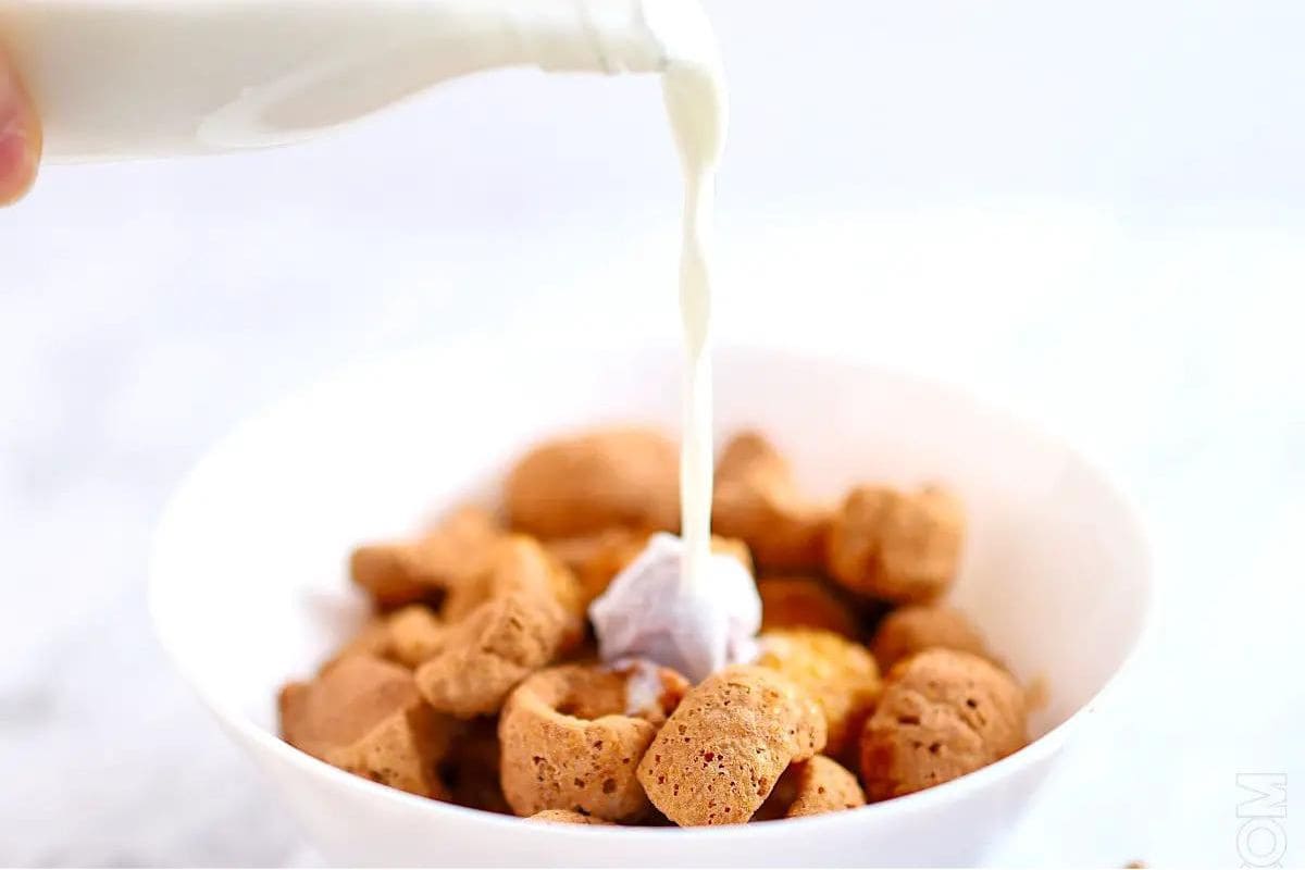 Milk being poured over a bowl of cereal.