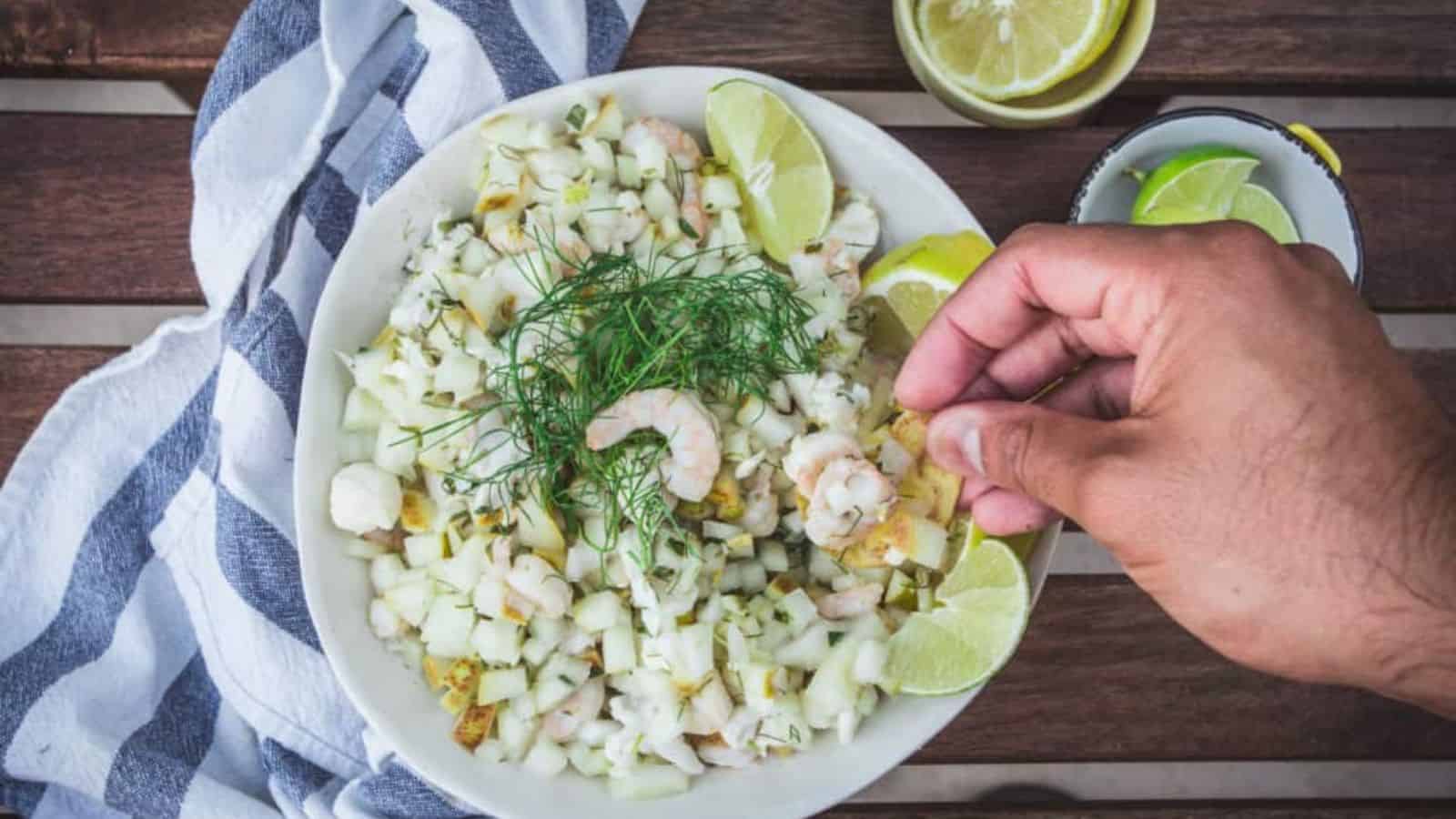 A hand is dipping a lime into a bowl of seafood salad.