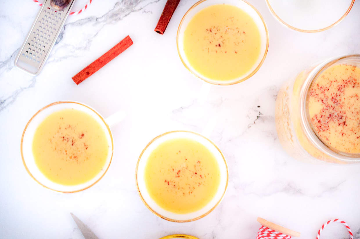 A top down shot of cups of eggnog and a jar of eggnog.