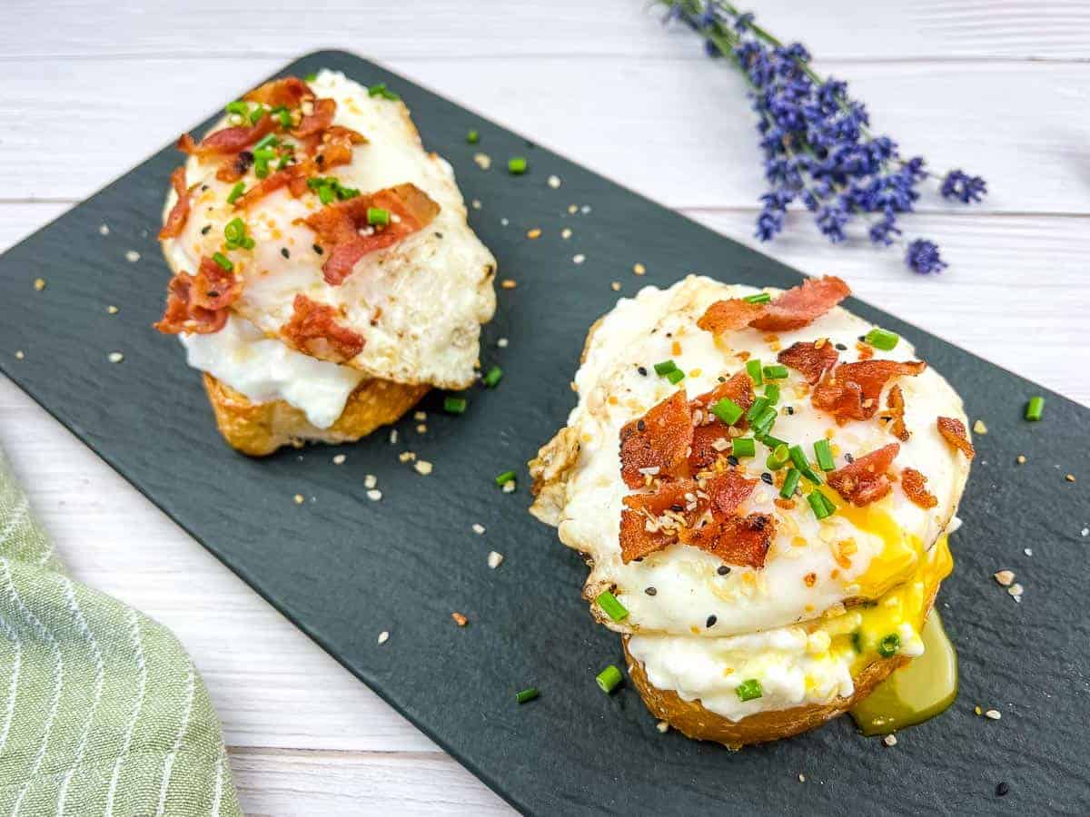 Two slices of Cottage Cheese Toast with Eggs & Bacon on a black platter.