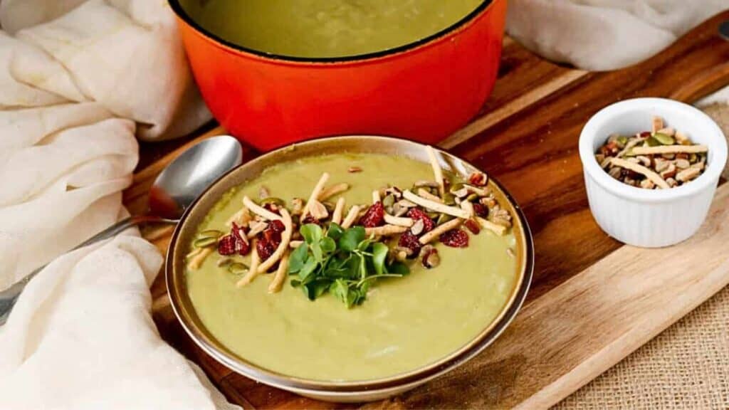 A bowl of soup and a pot on a wooden cutting board.