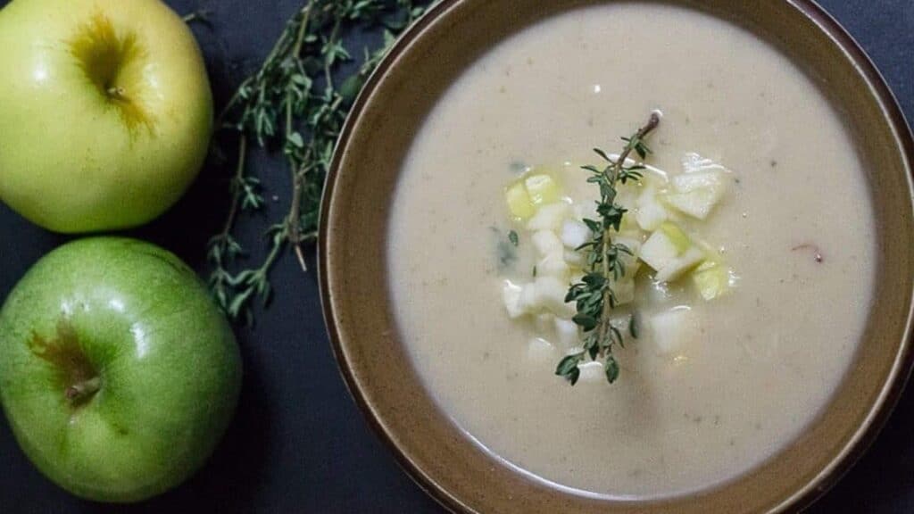 A bowl of soup with apples and sprigs of thyme.