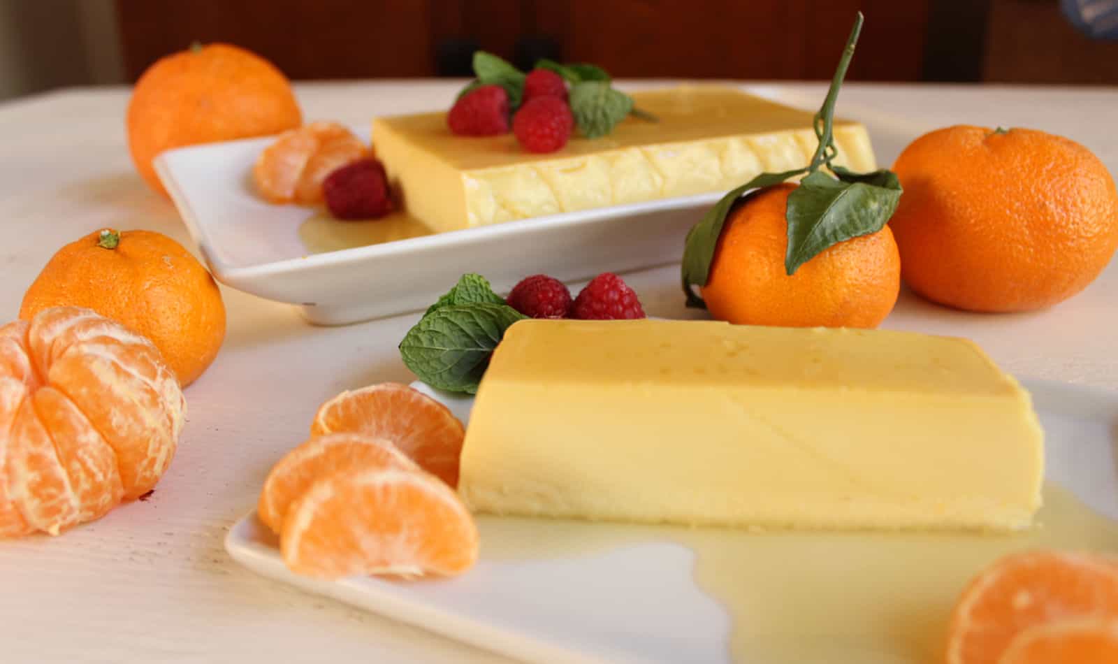 A plate with a piece of orange caramel cream and oranges on it.