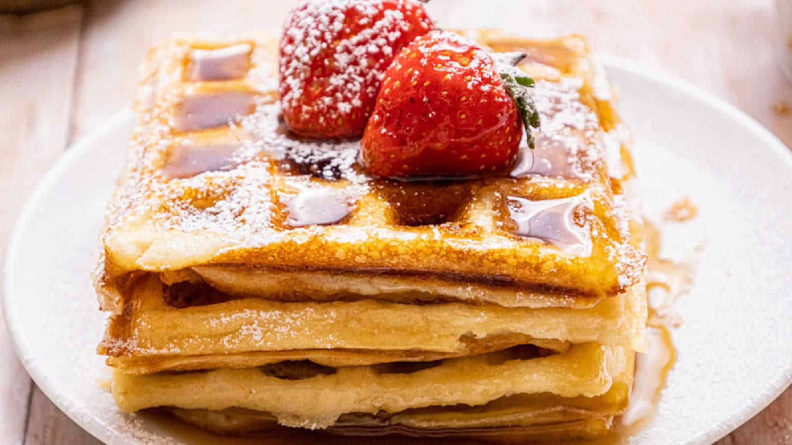 A stack of waffles with fruit and pouring syrup.