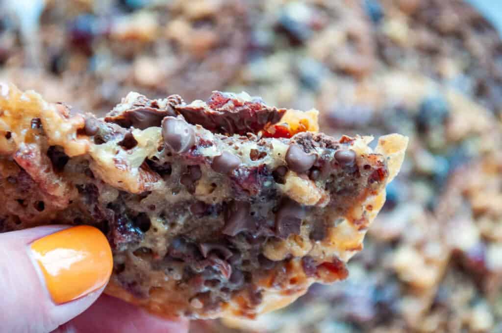 A person holding up a piece of chocolate chip cookie.