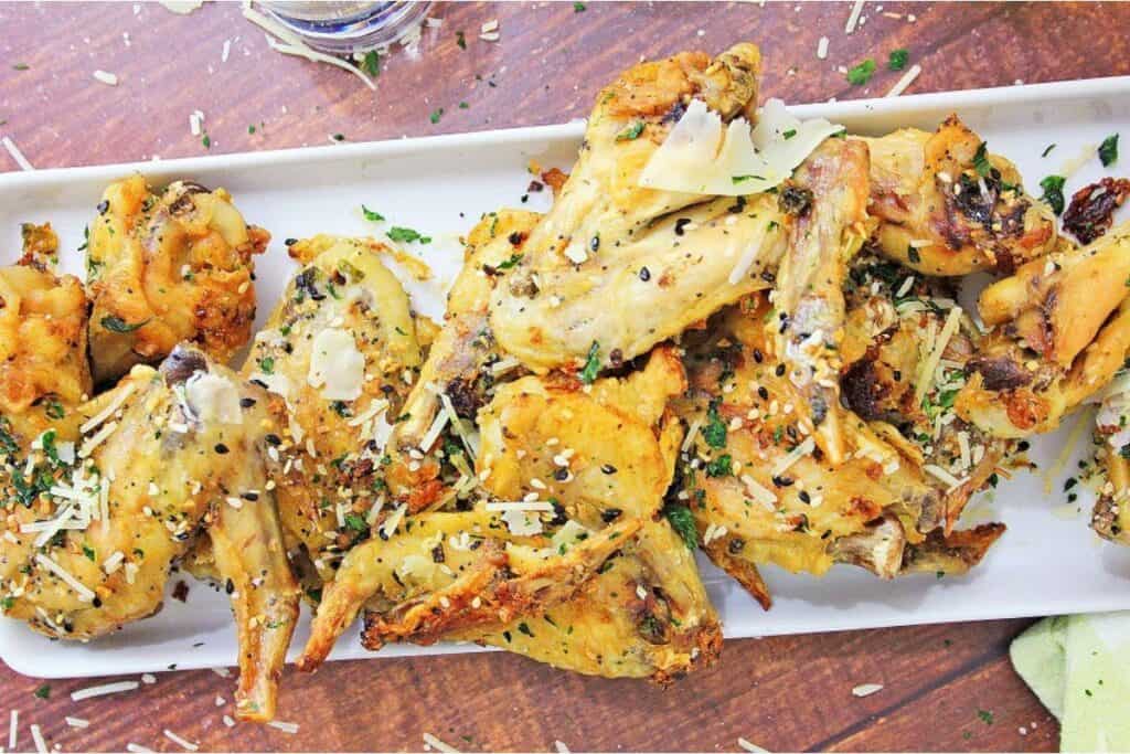 Chicken wings on a white plate with parmesan cheese.