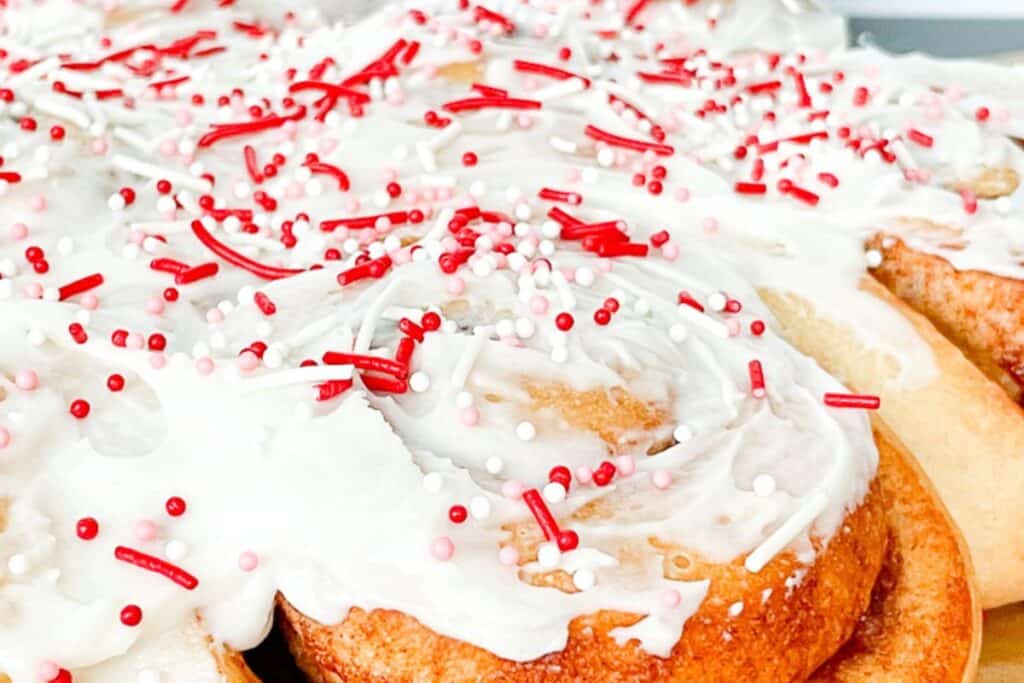 A plate of cinnamon rolls with icing and sprinkles.