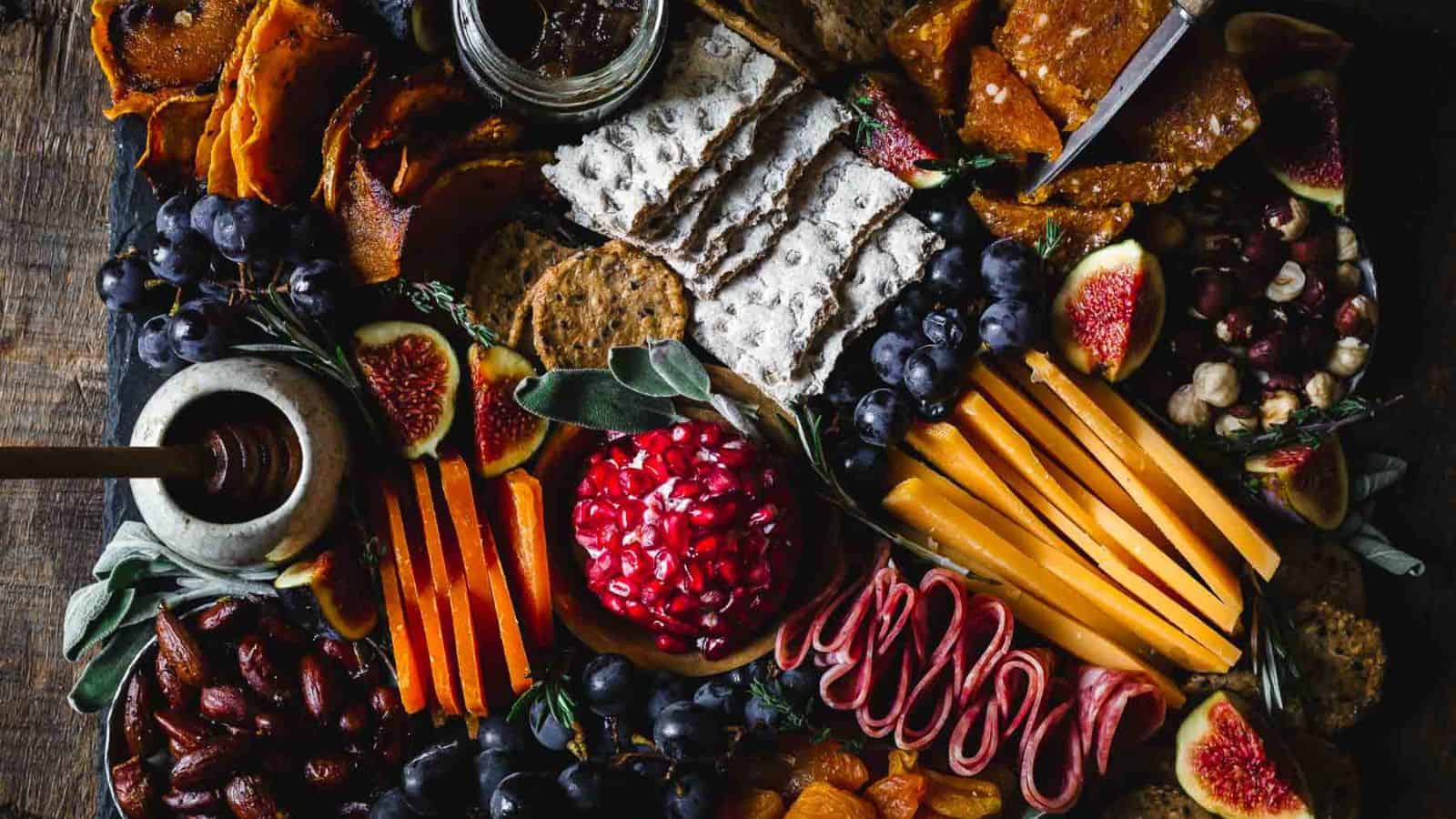 A platter of fruit, nuts, cheese and crackers on a wooden table.