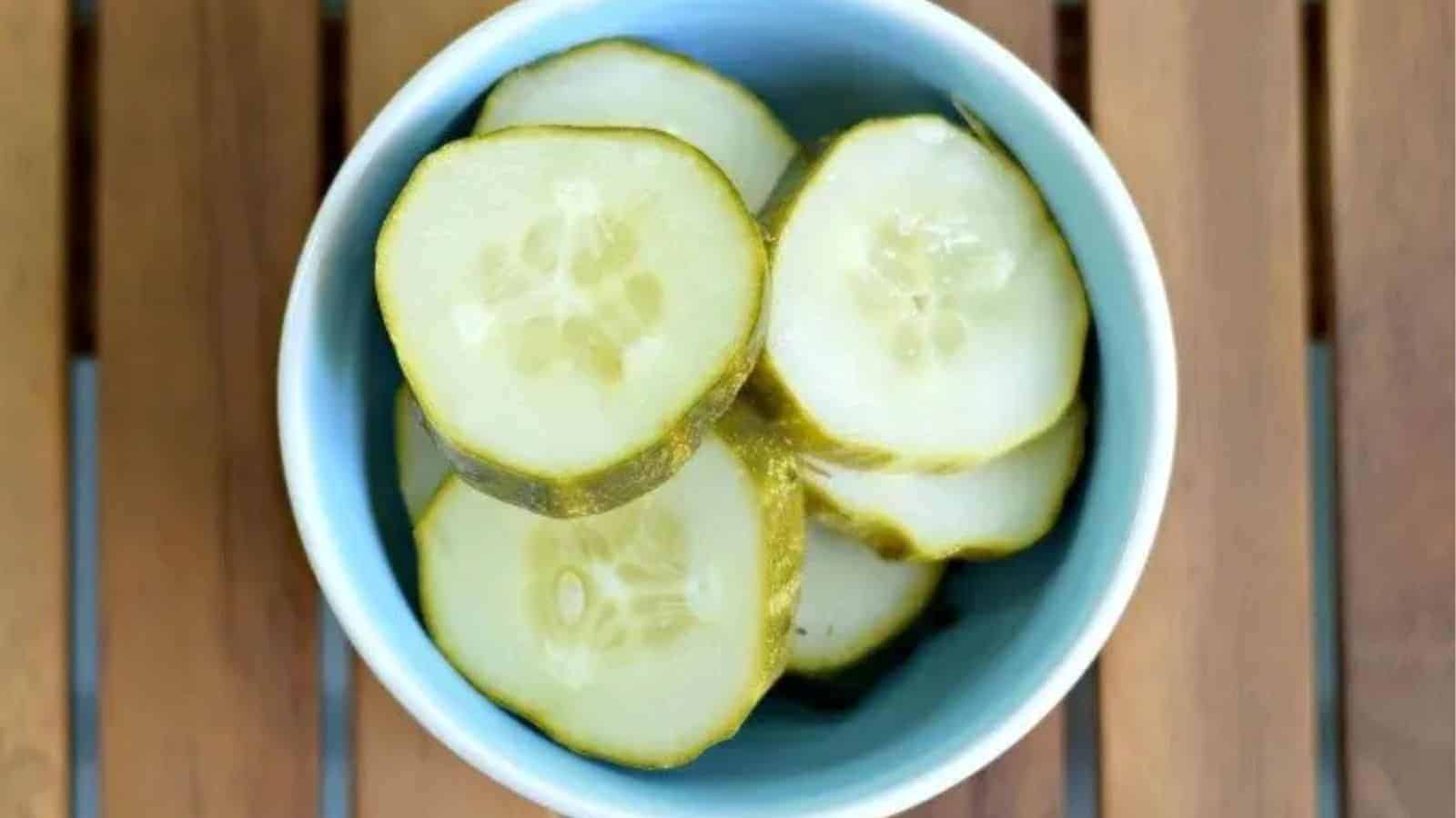 Image shows an overhead shot of sliced garlic dill pickles in a small dish sitting on a wooden board.