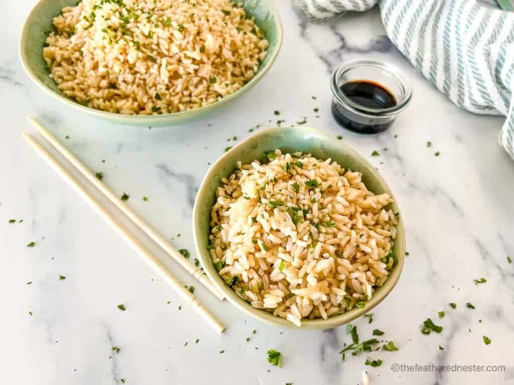 Two bowls of brown basmati rice next to a pair of chopsticks.