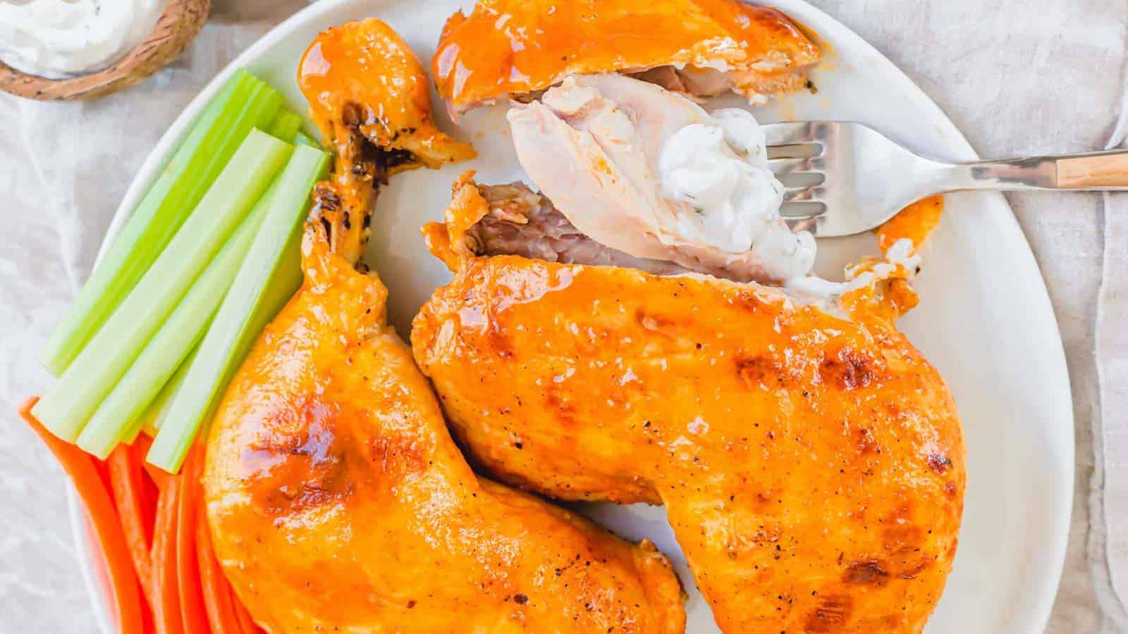 Instant Pot buffalo chicken leg quarters on a plate with celery, carrots and a creamy dipping sauce.