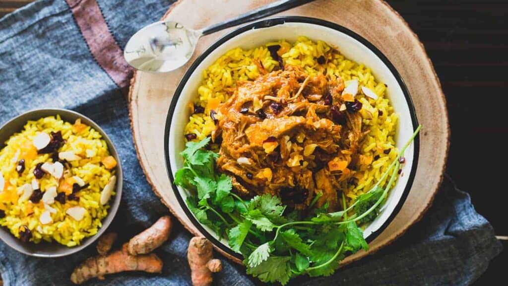 A bowl of rice, pork and curry on a wooden table.