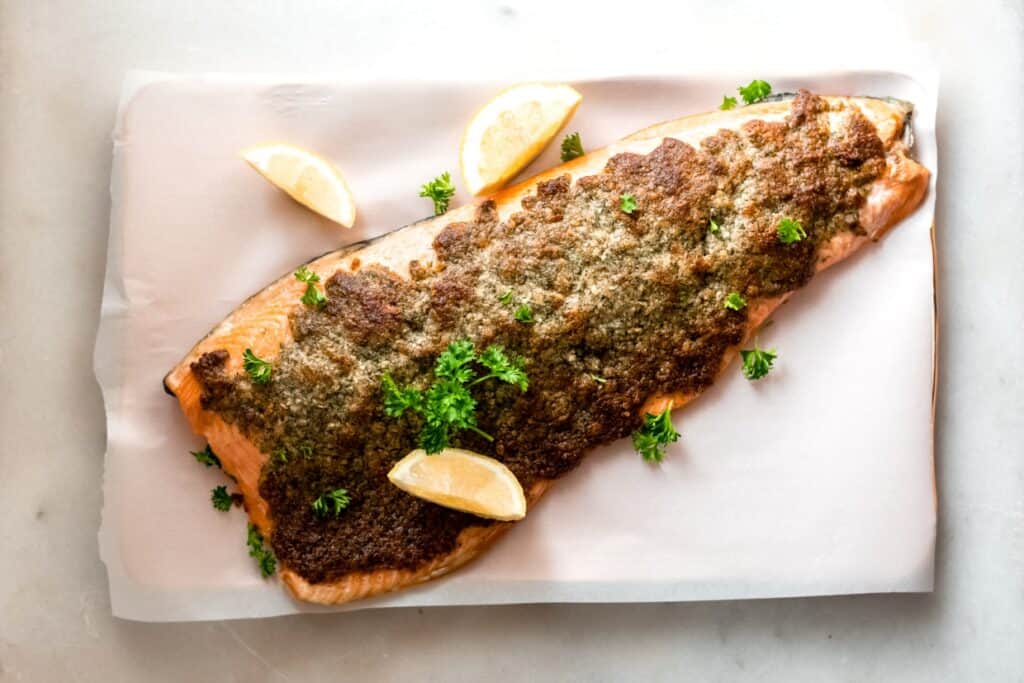 Baked Parmesan salmon on a baking sheet with lemon wedges.