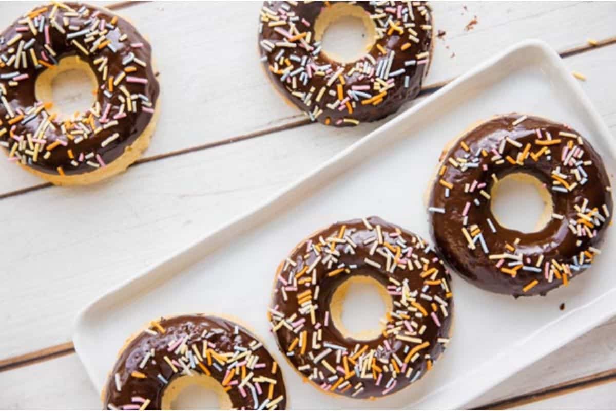 Five chocolate donuts with sprinkles on a white plate.