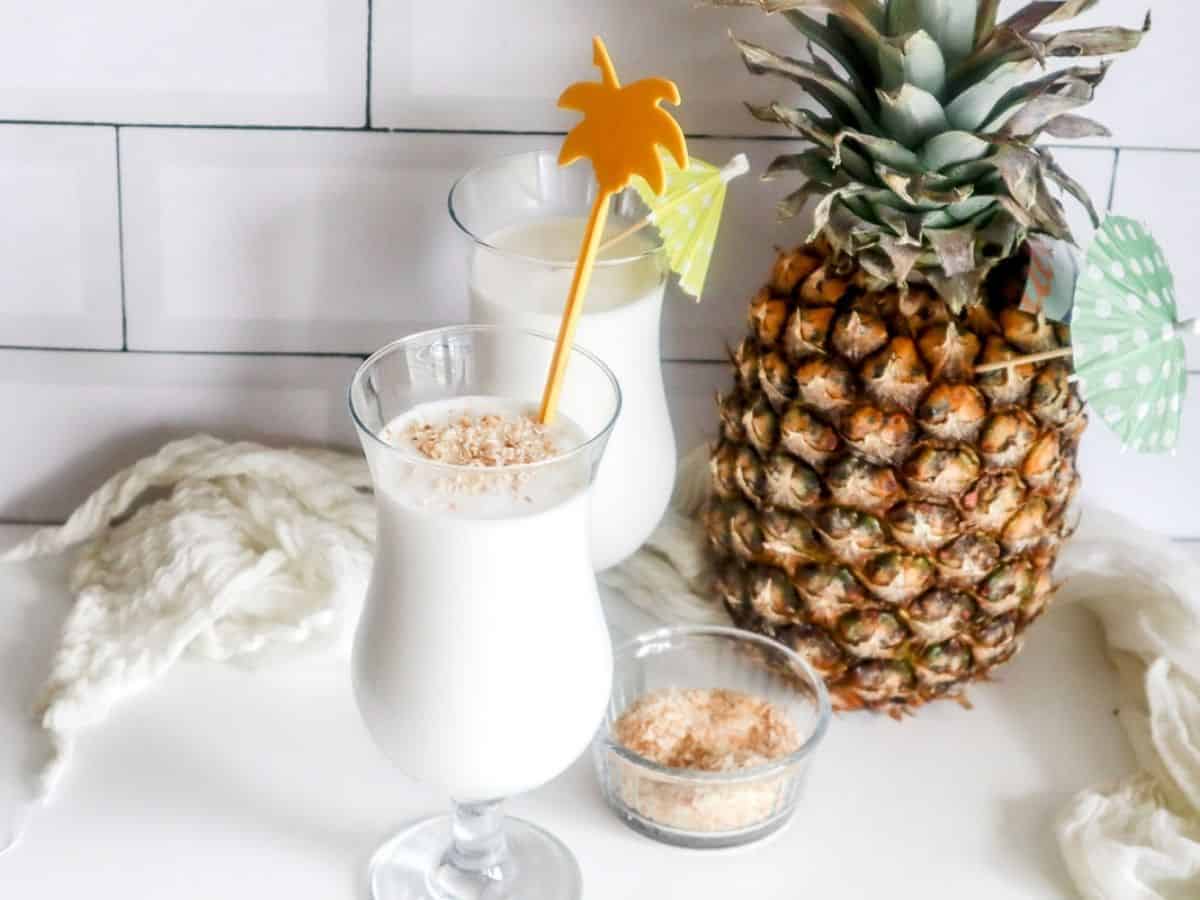 Two glasses of pina colada with a pineapple on top.